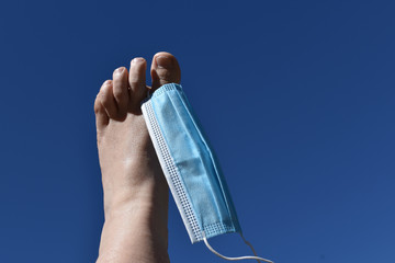 Mundschutz gegen Corona, Covid-19, flattert im Wind an Zehe hängend