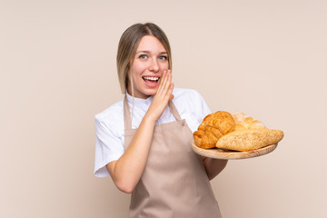 Young blonde girl with apron. Female baker holding a table with several breads whispering something