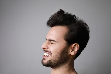 Close-up portrait of 30-year-old laughing man standing over grey background. Copy-space. Studio shot.