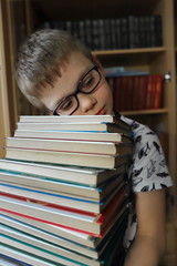 a boy with glasses holds a stack of books textbooks, a child is tired of the load at school, a student misses school during quarantine, coronavirus