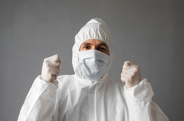 Doctor in white protective suit, medical mask and rubber gloves is showing Fig sign to the virus. Helping a people while coronavirus pandemic threat. Epidemic, pandemic of coronavirus covid 19.