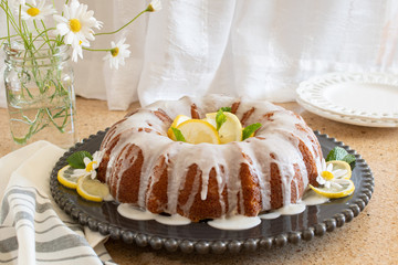 Lemon Ricotta Bundt Cake with icing displayed on a black decorative plate in a light bright airy setting.