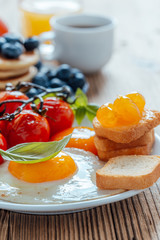 Homemade fried eggs with tomatoes, fresh summer fruits, berries, coffee and juice