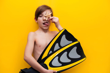 Travel and vacation background. Close up of a 9 years old boy with swimming flippers in his hands. Yellow background. Cheerful boy is going on a trip