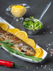vertical view to bakes trout on plate with sauce and green sprouts with pepper