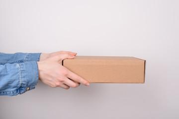 Dontion concept. Cropped profile close up photo of stretching to the side arms holding rectangular carton craft paper box isolated over grey background with copy space