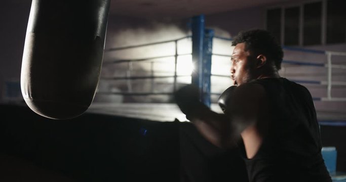 African american athlete is training in a gym, hitting a punching bag in boxing gloves, keeping fit before a fight - sports, active lifestyle concept 4k footage
