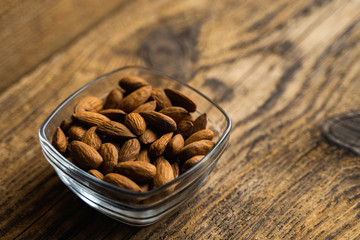 Almonds in a small plate on a vintage wooden table as a background with a copy space. Almond is a healthy vegetarian protein nutritious food. Natural nuts snacks.