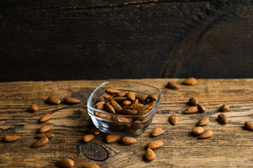 Almonds in a small plate with scattered nuts of almonds around a plate on a vintage wooden table as a background. Almond is a healthy vegetarian protein nutritious food. Natural nuts snacks.