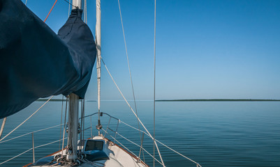Bow of a sailboat on still water with land visible on a distant horizon.