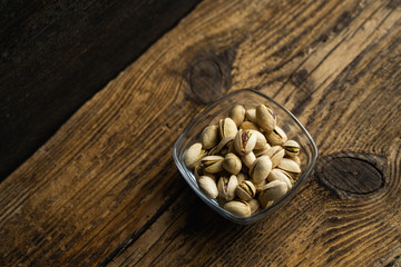 Pistachios in a small plate on a vintage wooden table as a background with a copy space. Pistachio is a healthy vegetarian protein nutritious food. Natural nuts snacks.