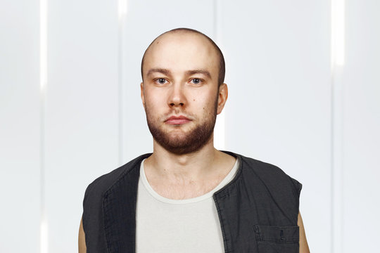 Portrait Young bald guy with beard with pocker face dressed in sleeveless shirt. Isolated on white background.