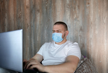 Man in medical mask with a laptop in the house. Coronovirus and home office