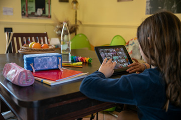 caucasian little girl smart studying at home during quarantine, using tablet, looking at screen, doing school tasks at home, distance education and home schooling in virtual classroom