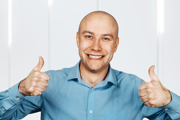 Portrait White bald guy in blue shirt showing thumbs up and smiling