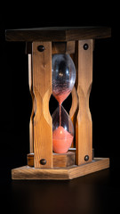 old dusty wooden hourglass with pink sand. black background.