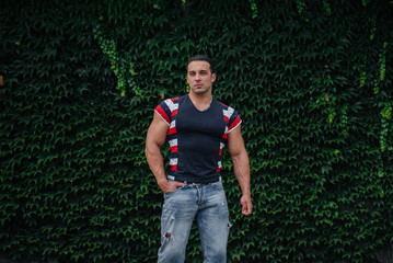 A sporty guy is sitting near a green wall of plants. Ecology