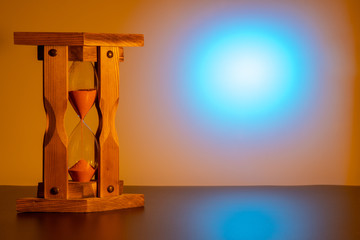 an old wooden hourglass  in the left part of the frame. the time is running. blue round spot on the...