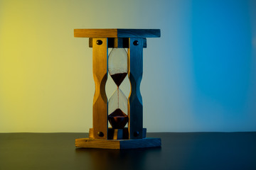 running wooden hourglass in the shade. Time goes on. yellow-blue linear gradient background.