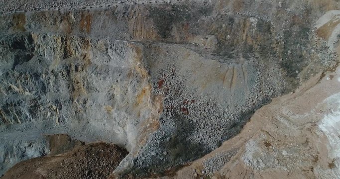 Aerial footage of a steep rock wall at a quarry. It shows mine terraces and landslide