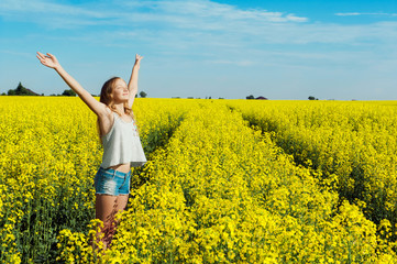 Naklejka na ściany i meble Happy girl with wide open hands in a yellow flowering field on a sunny day experiences a feeling of joy and freedom
