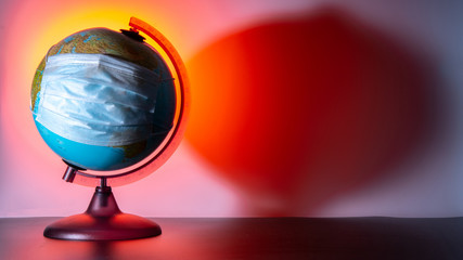 A globe of the Earth with a medical mask on it. Orange background. Dark shadow from the globe. Coronavirus pandemic. World medical concept. Concept of fight against virus.