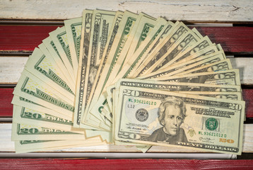 Thousands of US dollars laid out in a fan shape with 20 dollar bills on wooden USA flag