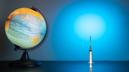 Globe of the earth in a medical mask. World quarantine, coronavirus pandemic. Planet Earth with face mask protect. World medical concept. Blue gradient background. The syringe stands vertically