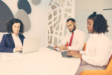 Serious business people with laptops and papers. Group of professional multiethnic business colleagues working with computers and documents in office. Business concept