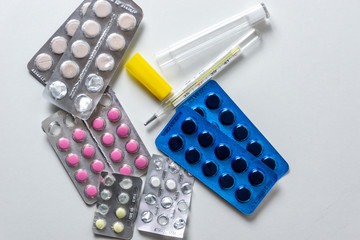 Pills and thermometer lying on a white table without boxes, medicines that are used to treat