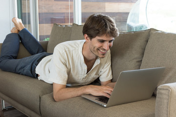 Jeune homme travaillant sur son ordinateur portable allongé sur le canapé