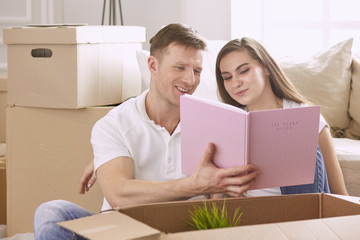 Portrait of happy couple looking at laptop computer together sitting in new house, surrounded with boxes