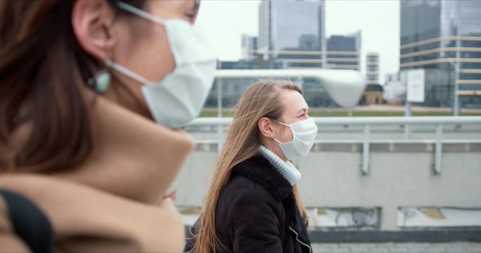 Epidemic Protection. Two Young Happy Caucasian Business Women Wear Face Masks Walking On City Street During Quarantine.