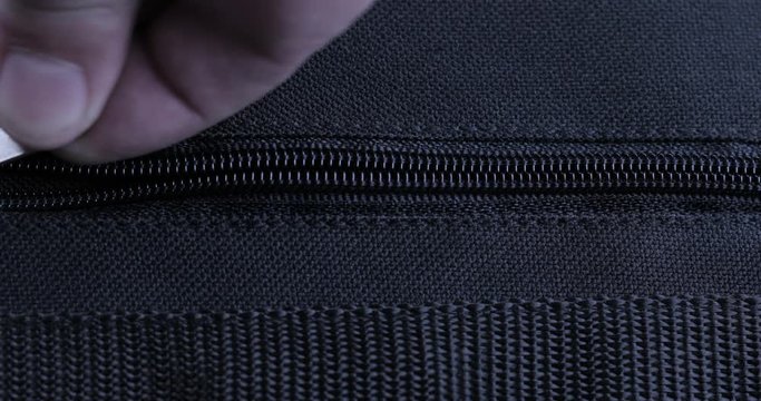 A hand closing a zipper of a black bag
