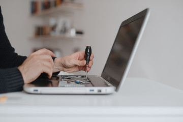 A man disassembles a laptop. Computer service and repair concept. Laptop disassembling in repair shop, close-up. Electronic development, electronic device fixing
