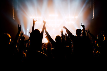 Crowd of people with raised up hands to the stage. Silhouettes in bright stage lights.