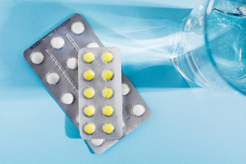 Two blister of pills with glass of water over blue background. Top view