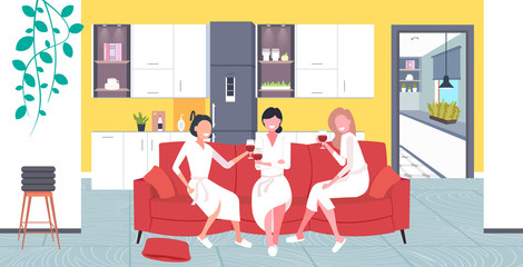 beautiful women in bathrobes drinking wine having fun home care concept girls sitting on sofa relaxing during bachelorette party modern kitchen interior full length horizontal vector illustration