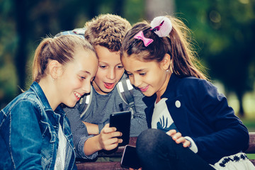 Group of happy friends hang out after school and using smart phone, watching funny video while sitting on the bench