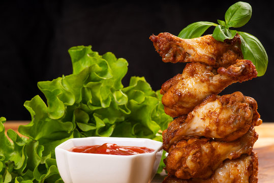 Delicious Crispy Chicken Wings In Bread Crumbs With Ketchup And With Tomatos.Fried Breaded Chicken Wings On A Black Background .