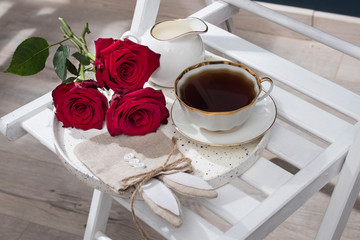 Three red burgundy roses, a cup of tea and a bag for gifts in the form of a hare for Easter on a tray. Breakfast.