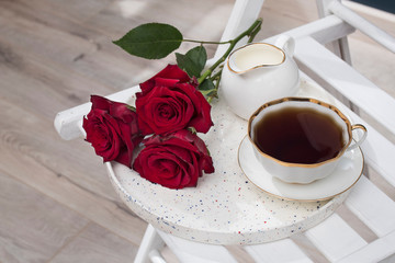 Three red burgundy roses, a cup of tea and on a tray.