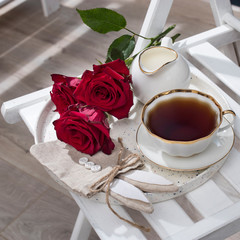 Three red burgundy roses, a cup of tea and a bag for gifts in the form of a hare for Easter on a tray. Breakfast.