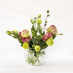 Bouquet of green and pink terry lisianthus and eucalyptus branches in a transparent round vase on a white background.