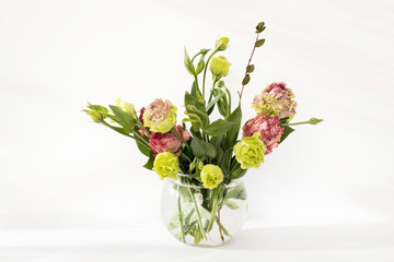 Fototapeta na wymiar Bouquet of green and pink terry lisianthus and eucalyptus branches in a transparent round vase on a white background.
