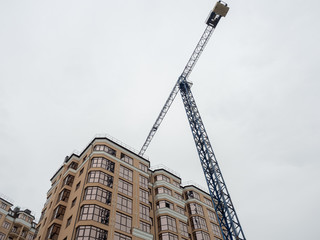 Fototapeta premium A blue tower crane stands next to a beige new home.