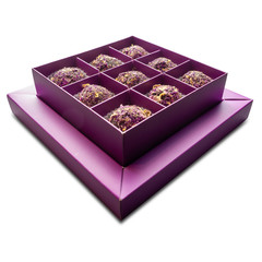 Angular view of candies sprinkled with dry rose petals lie in a purple box on an isolated background.