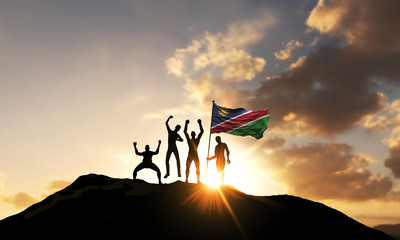 A group of people celebrate on a mountain top with Namibia flag. 3D Render