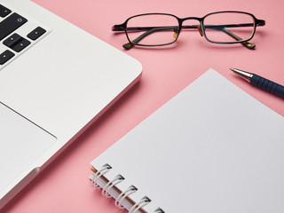 Flat lay, top view office table desk frame. Laptop, glasses, notebook notepad on pink background. Home Remote work education Coronavirus quarantin.