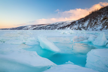 Beautiful winter landscape with sea, ice, and coast. Large cracks and water among ice floes and hummocks. Traveling and Hiking in nature. Sea of Okhotsk, Magadan Region, Siberia, Far East Russia.